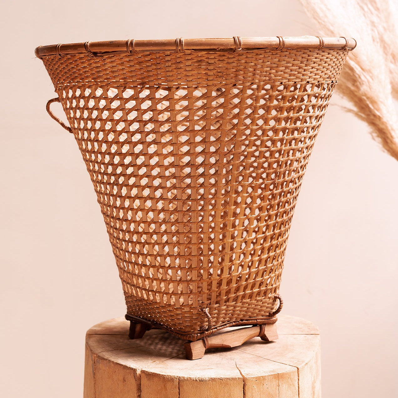 A handwoven cane and bamboo basket, primarily brown in color, displayed on a wooden stool.