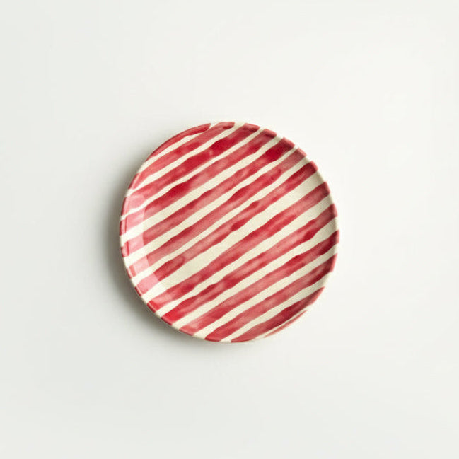 Round ceramic plate with red and white striped pattern on a light gray background