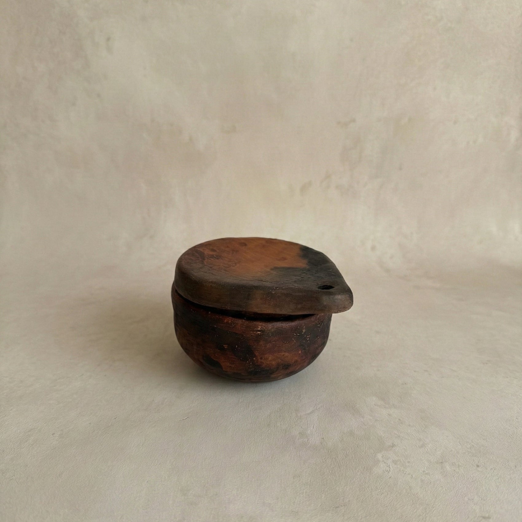 Small clay container with a lid on a beige background
