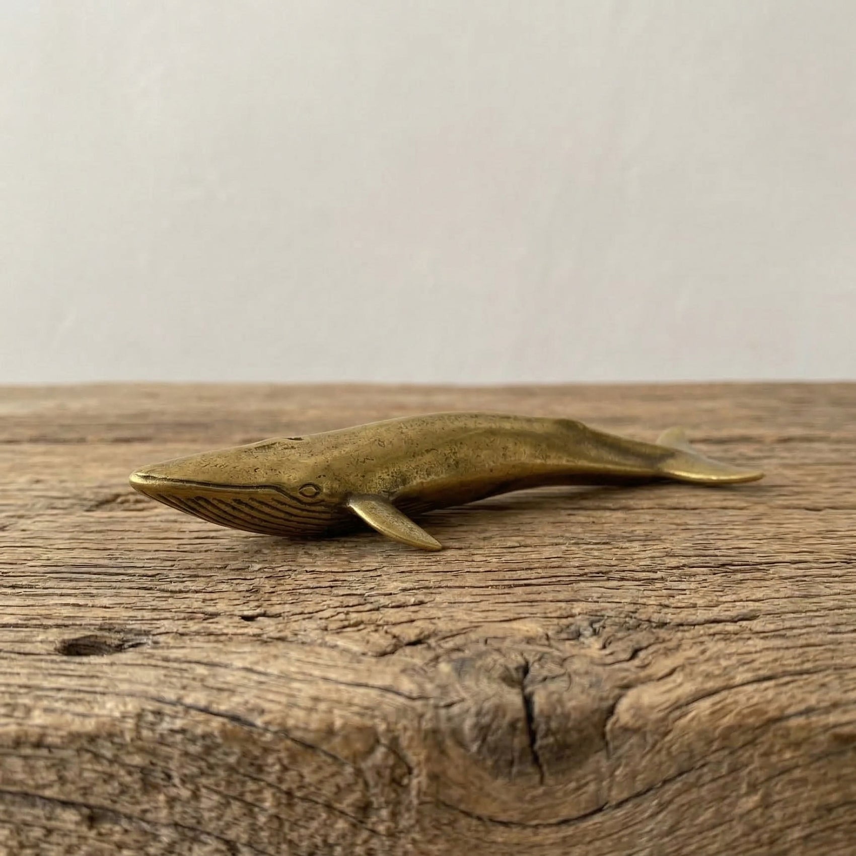 The Ancient Navigator miniature solid brass whale figurine with aged patina on natural stone surface