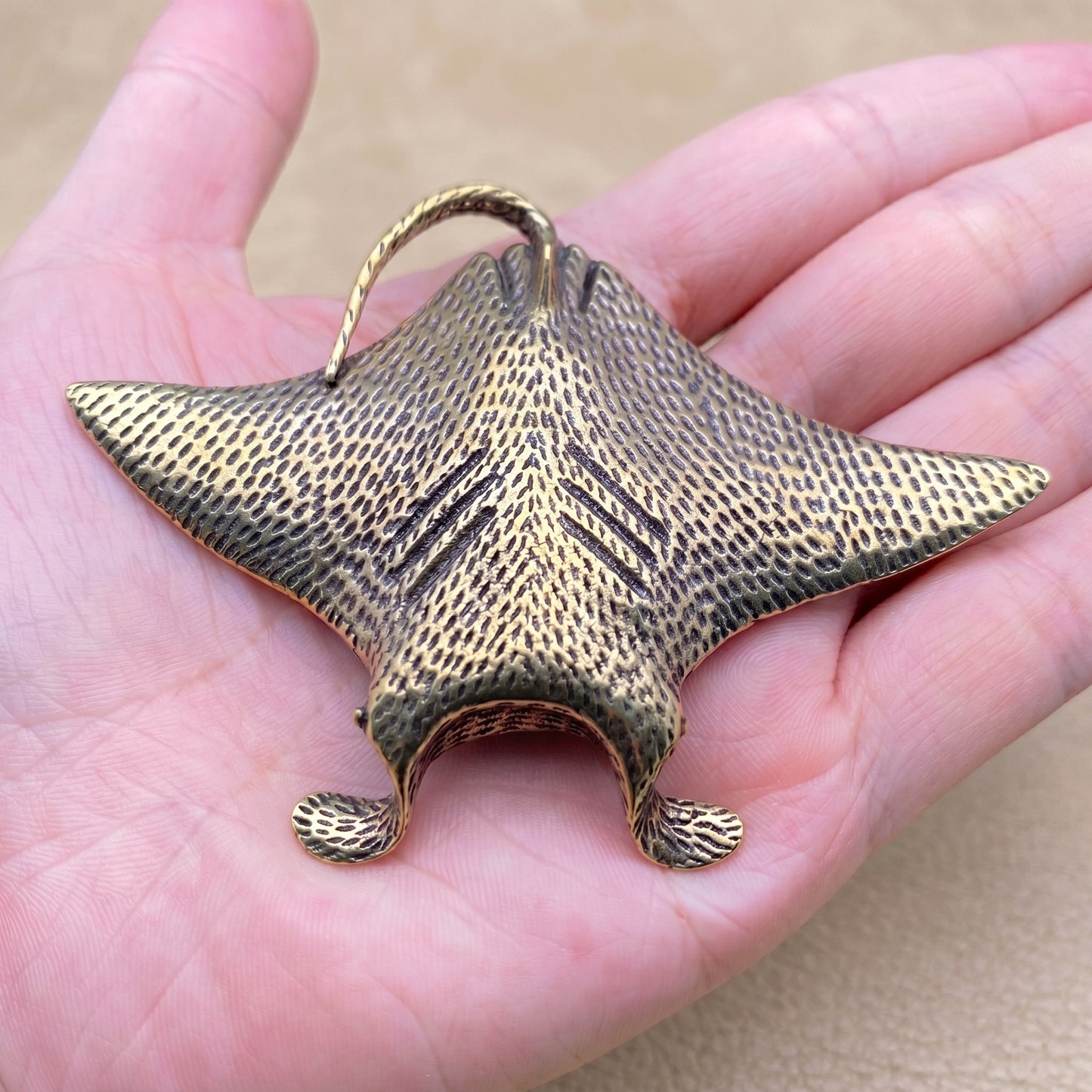 The Drifter brass manta ray held in a hand to show its size, about 3.3 inches across