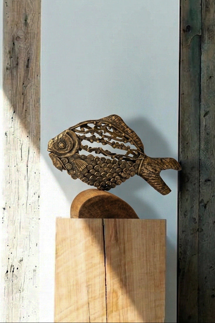 The Eternal Current Dhokra lost-wax cast metal fish sculpture by Rahul Dey displayed on a wooden pedestal in warm afternoon light, showing spiral scale detail and cast latticework, handcrafted in Kolkata India, from WILLAGE