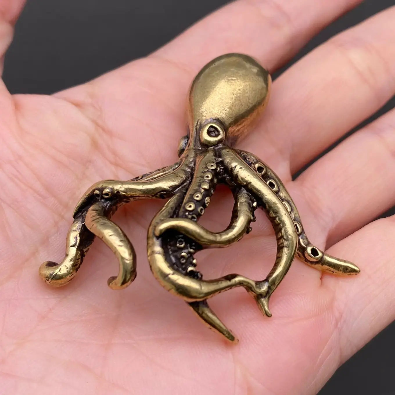 The Fluid Intellect miniature brass octopus held in hand to show scale, with curling tentacles and warm aged patina, from the WILLAGE Tiny Objects collection
