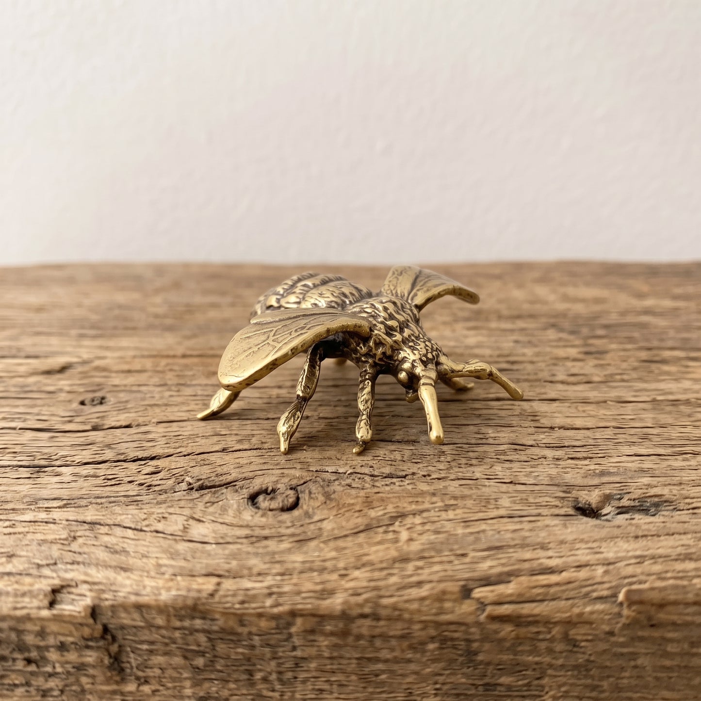 Brass bee figurine held in an open palm to show its palm-sized scale, veined wings, and textured thorax