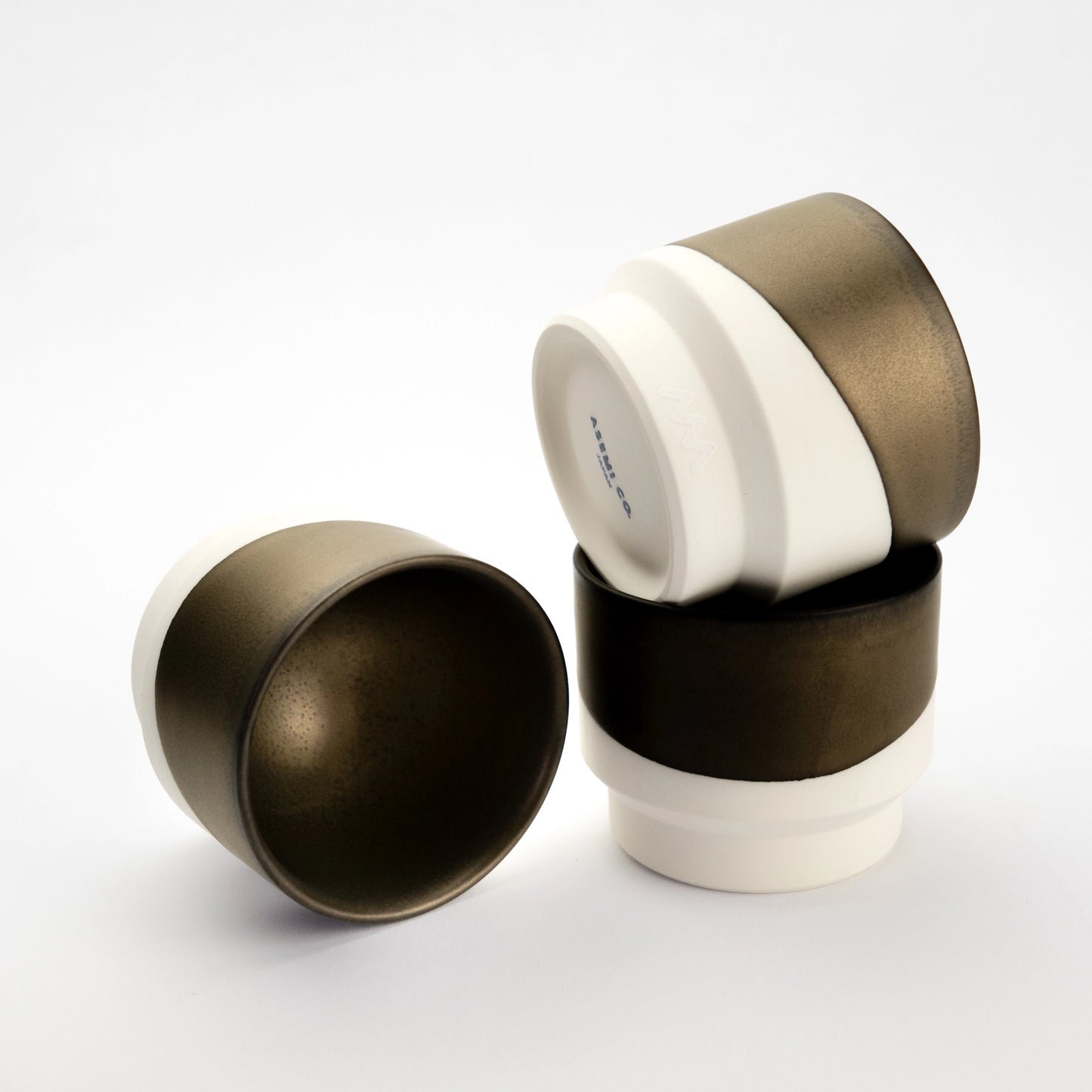 Three bronze-and-white Hasami porcelain cups stacked and angled to show the glazed interior and unglazed base