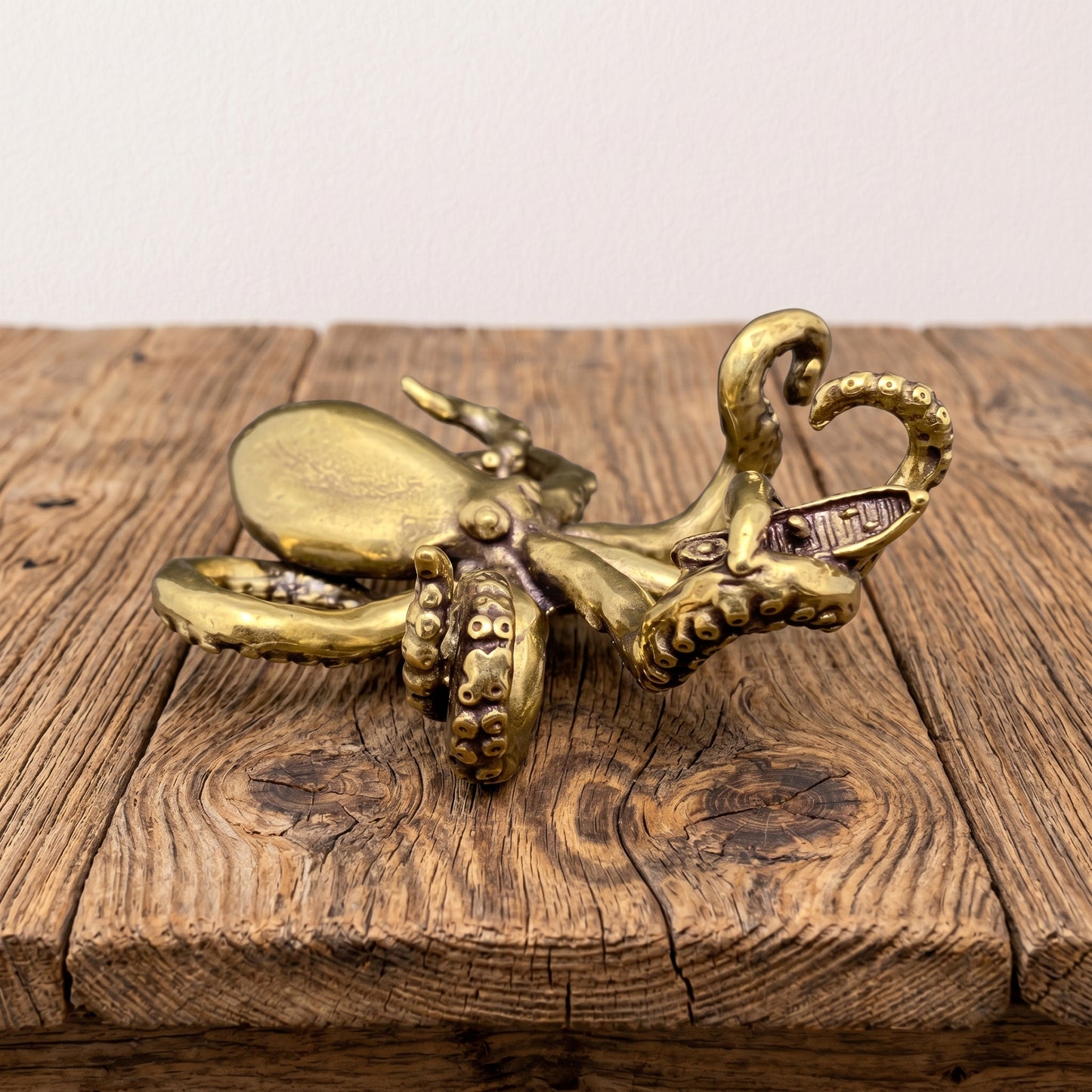 Solid brass octopus figurine with curling tentacles cradling a small boat, antique patina finish, shown on a clear stand against a gray background