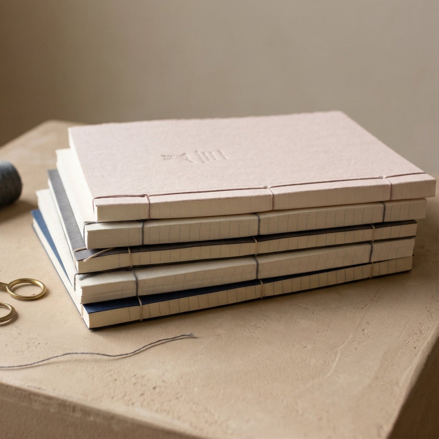Stack of WILLAGE hand-bound journals showing Japanese stab binding with thread and scissors on stone surface