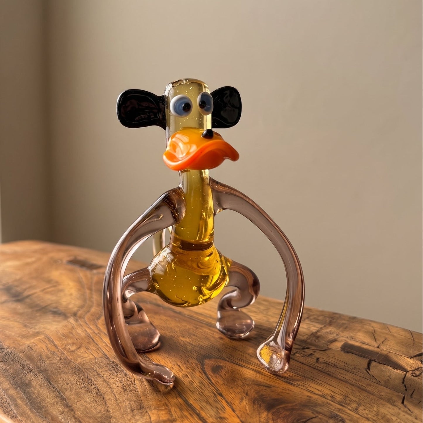 Front view of The Lanky Ape lampworked glass monkey figurine showing face detail with blue eyes, orange lips, and black floppy ears, amber solid glass by Glass by Iness