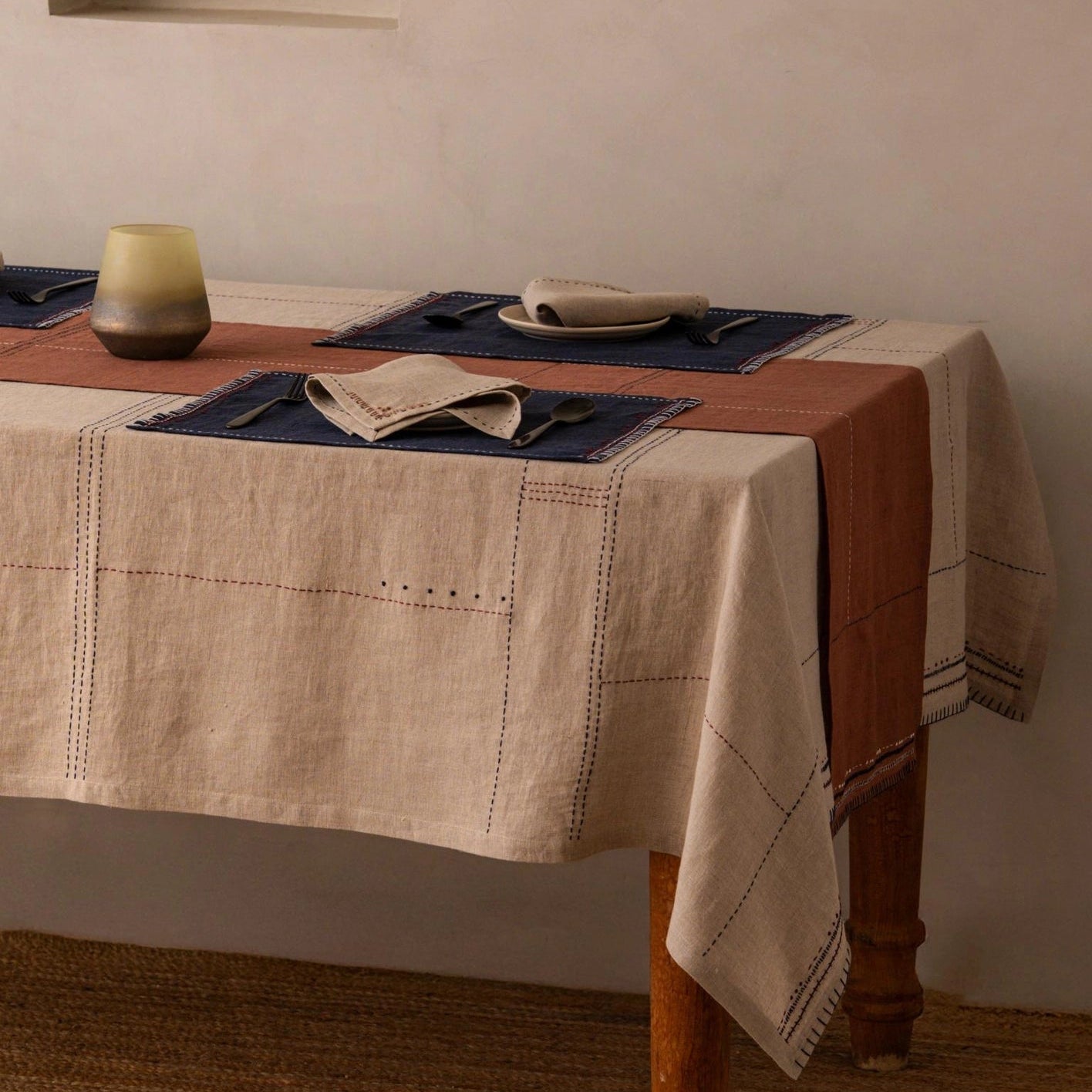 Close-up of hand-stitched dashed lines in navy and white thread on eucalyptus terracotta linen table runner, showing drape and fabric texture