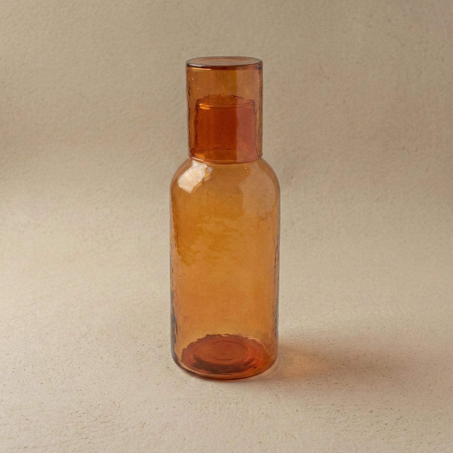 Hand-hammered recycled glass carafe in amber with tumbler lid, showing warm golden tones and hammered facets