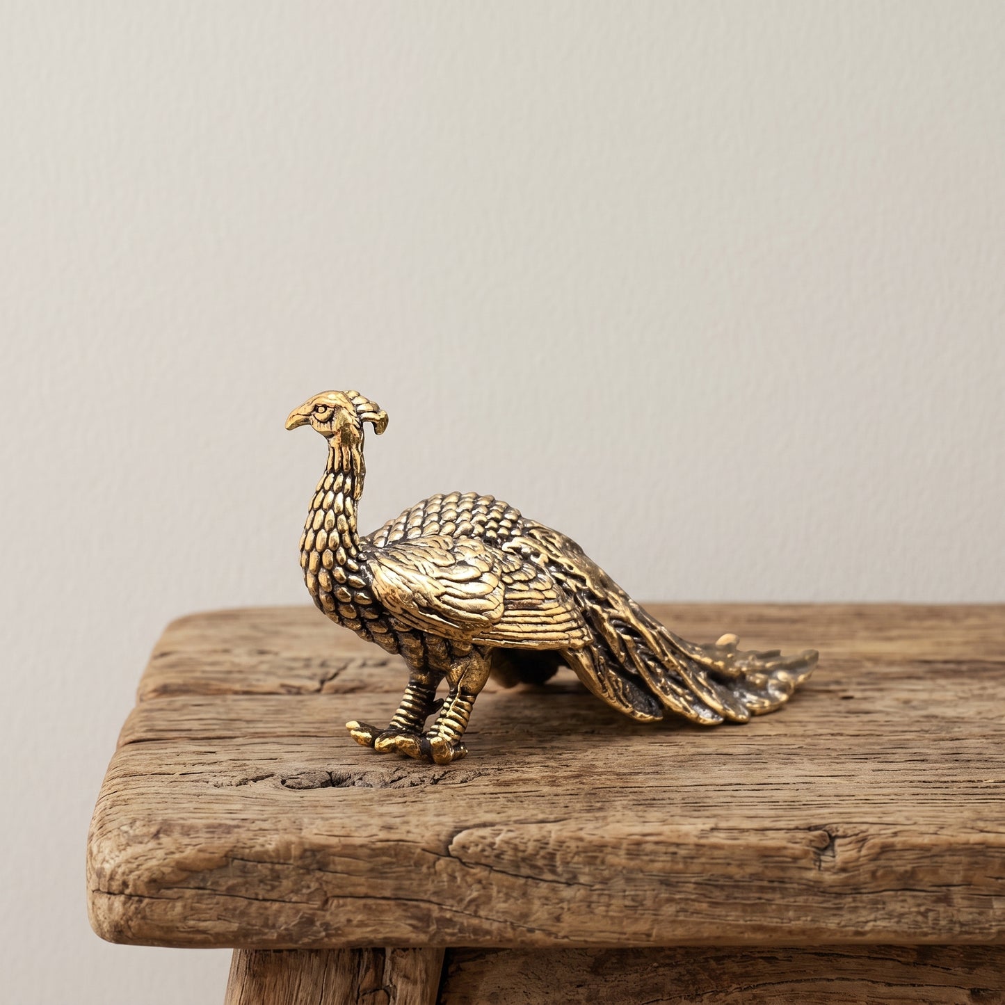Brass peacock figurine in profile with a long layered feather train and antique patina, on a clear acrylic stand