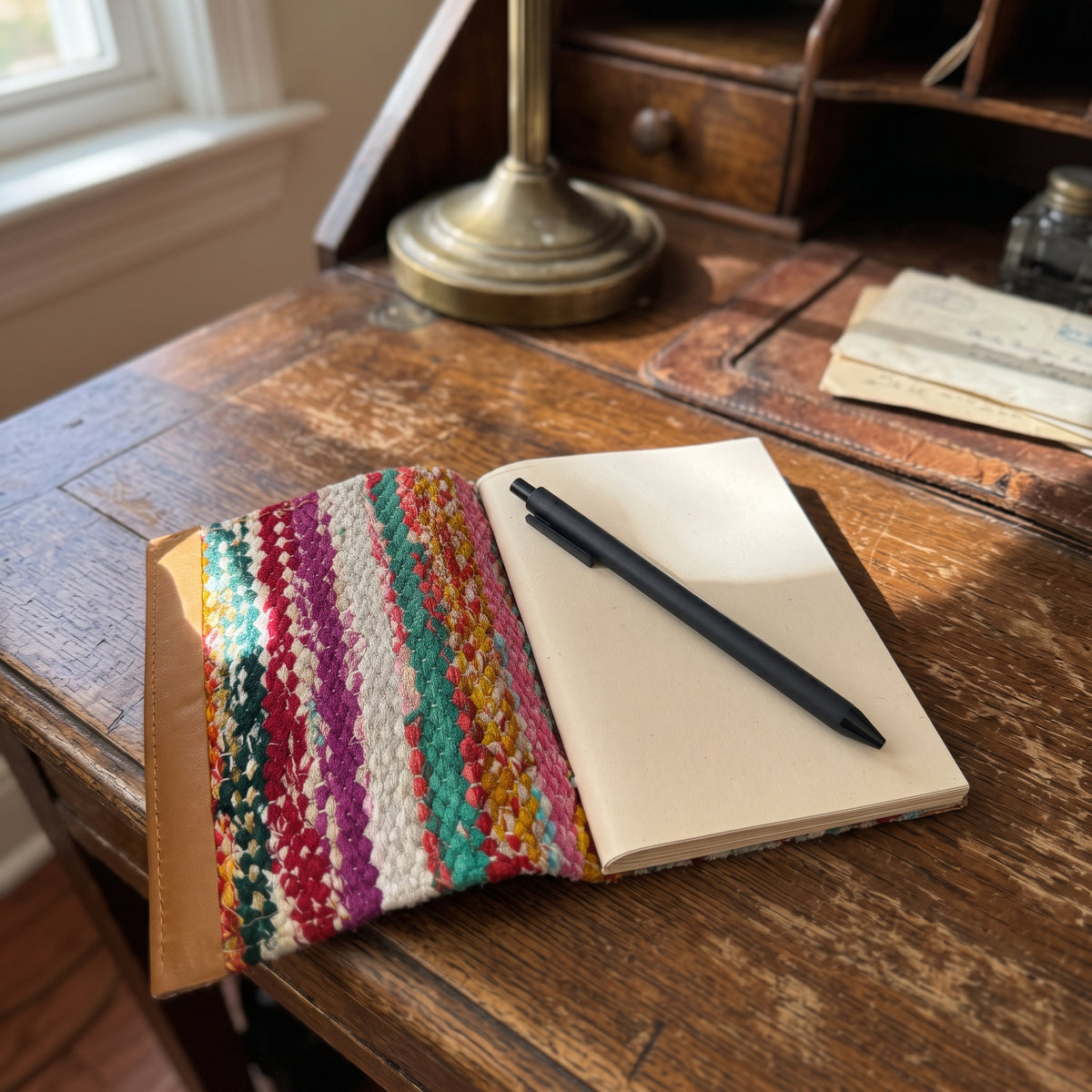 Woven sari journal lying open on a wooden writing desk with blank pages in warm window light