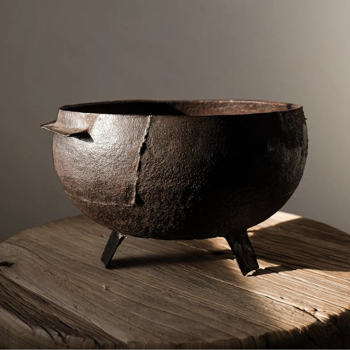 A vintage iron incense burner with a round shape and a single handle, placed on a wooden surface with a shadow falling over it.