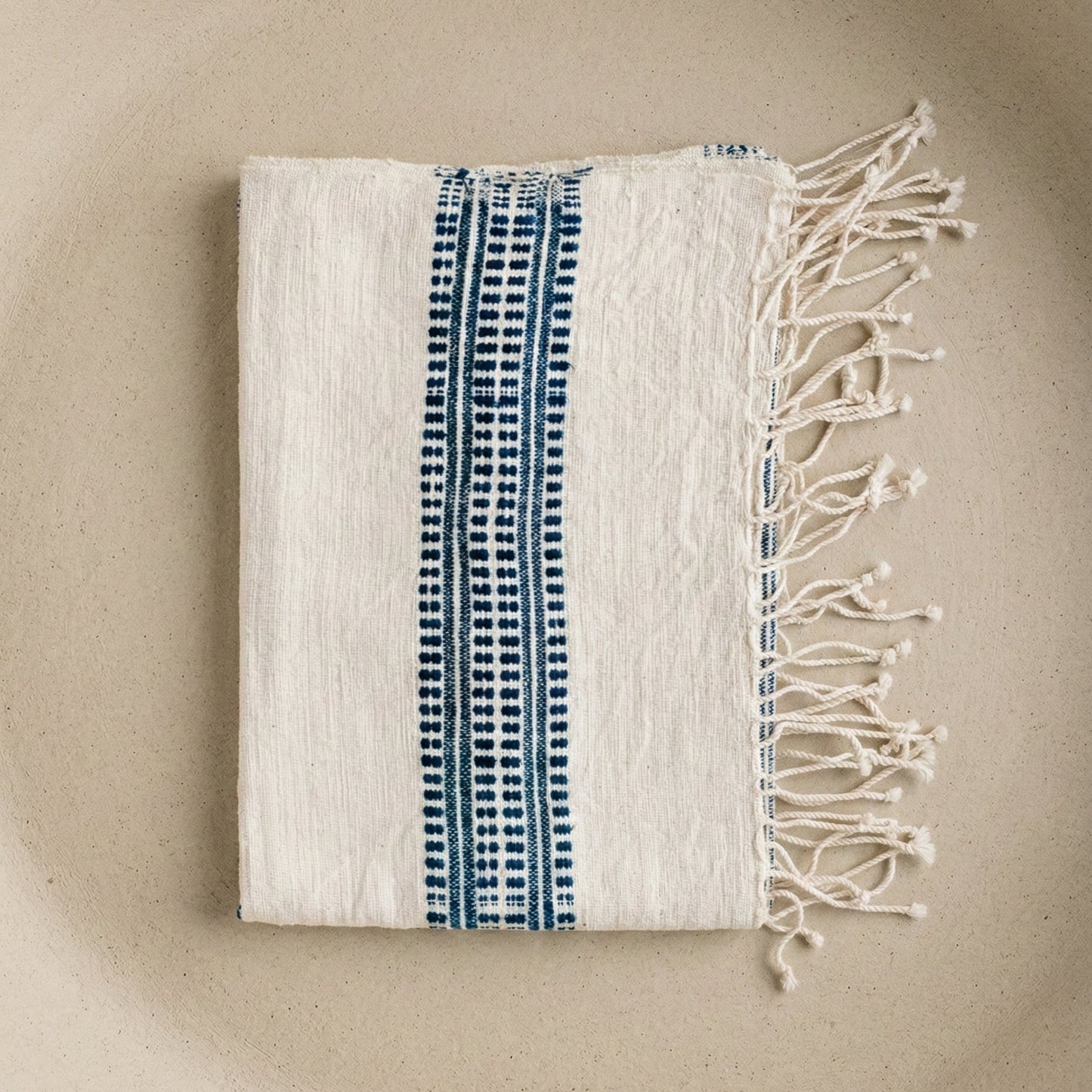 Folded towel with blue pattern and white fringes on a beige background