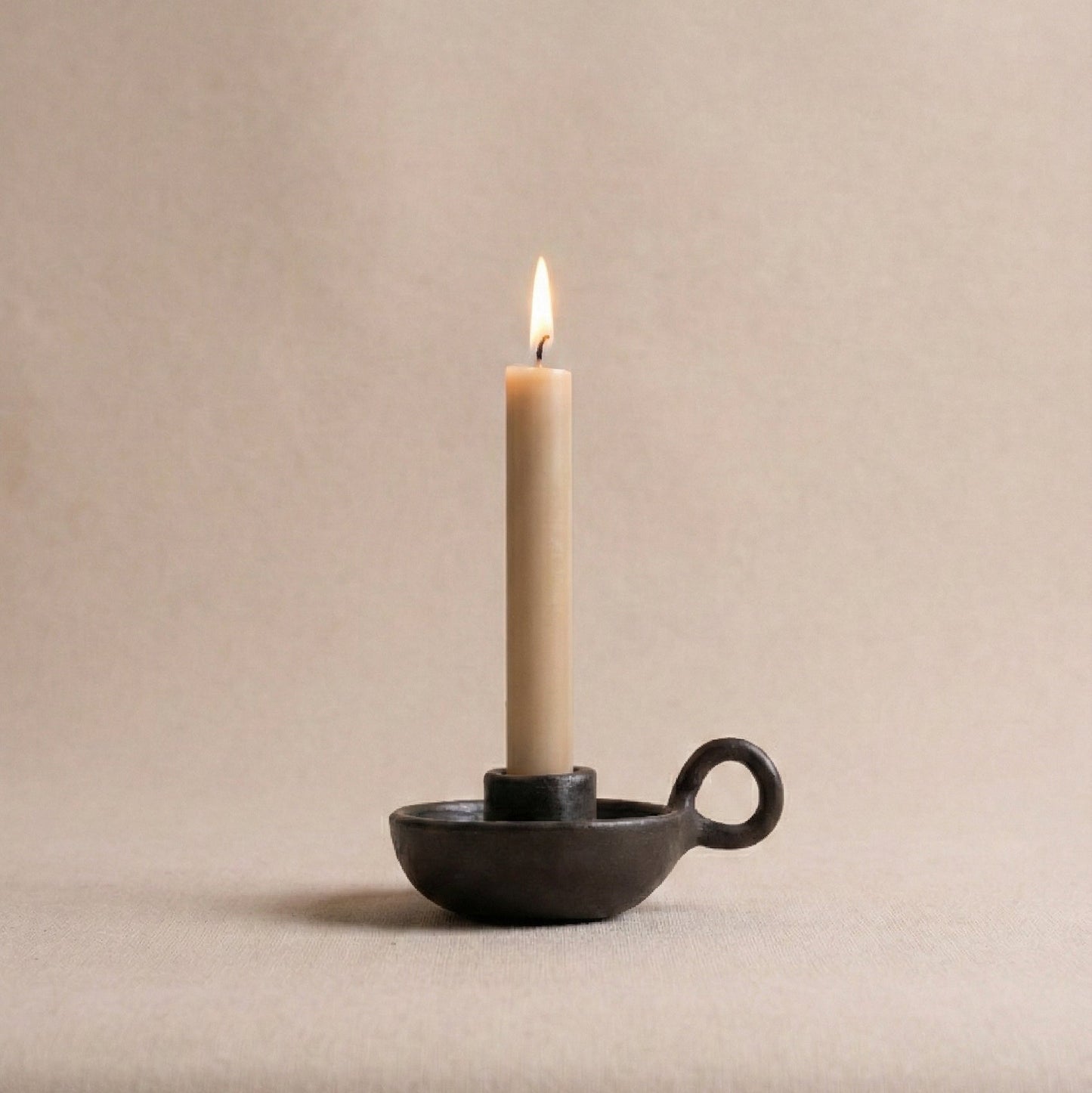 Black candle holder with a lit beige candle on a beige background