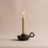Black candle holder with a lit beige candle on a beige background