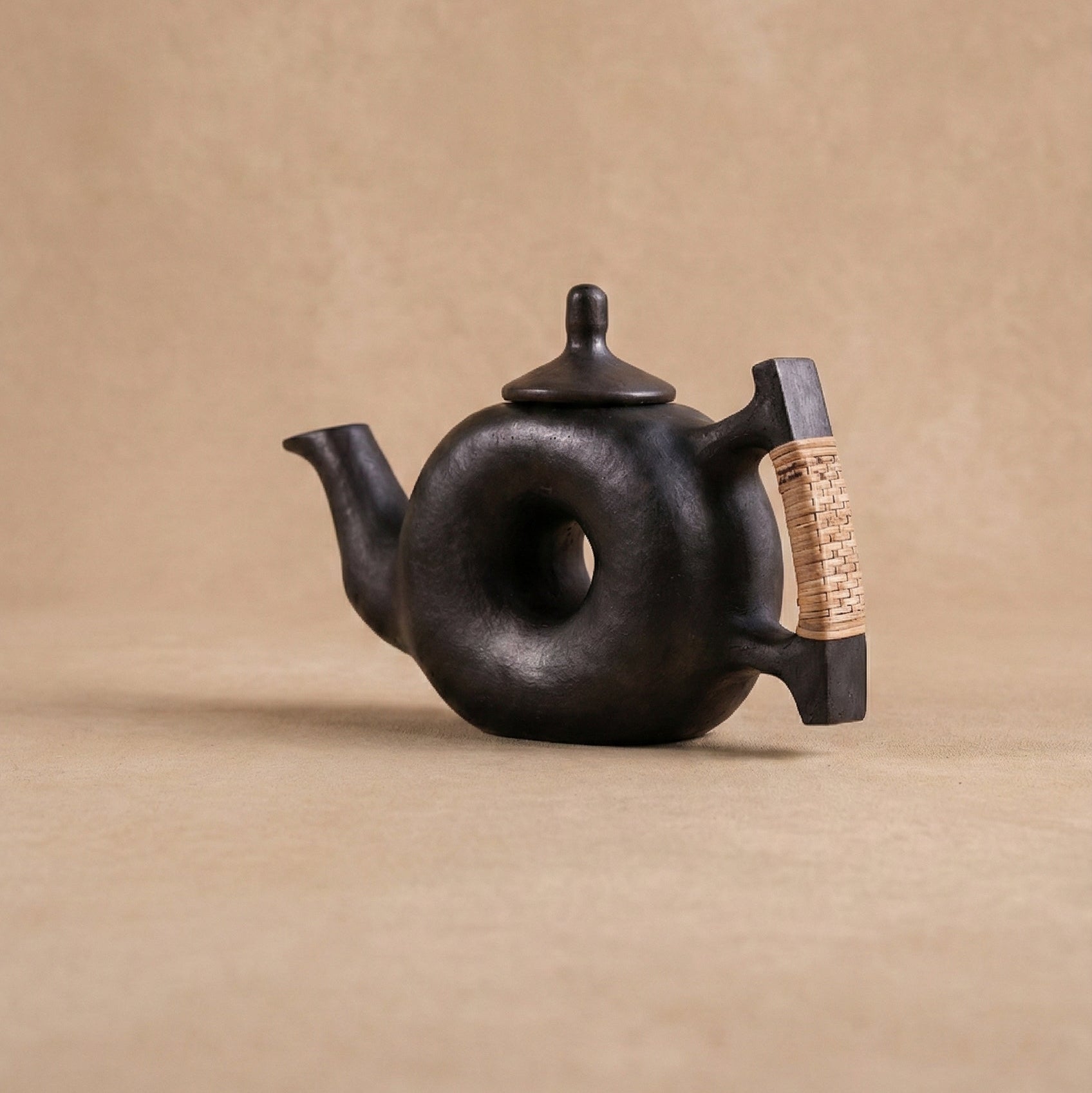 Black ceramic teapot with a textured handle on a beige background