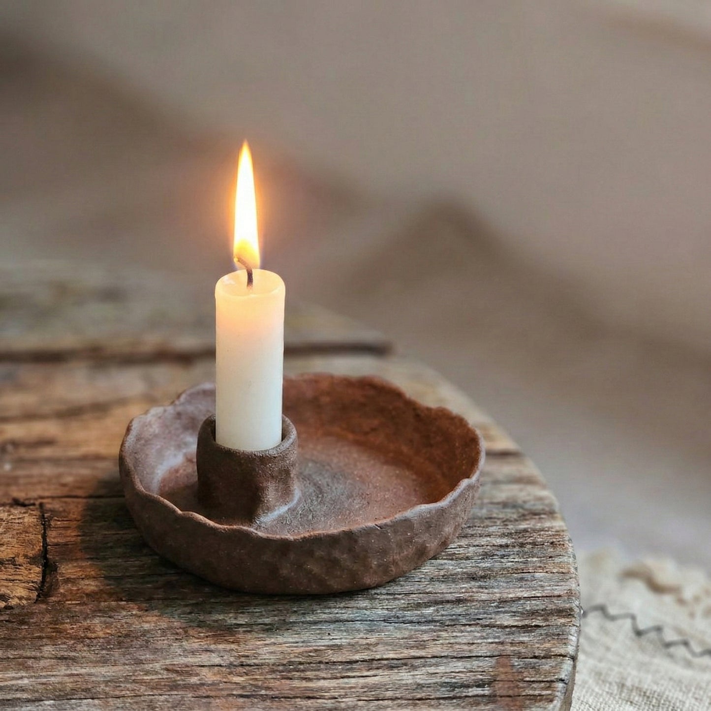 Candle in a rustic ceramic holder on a wooden surface