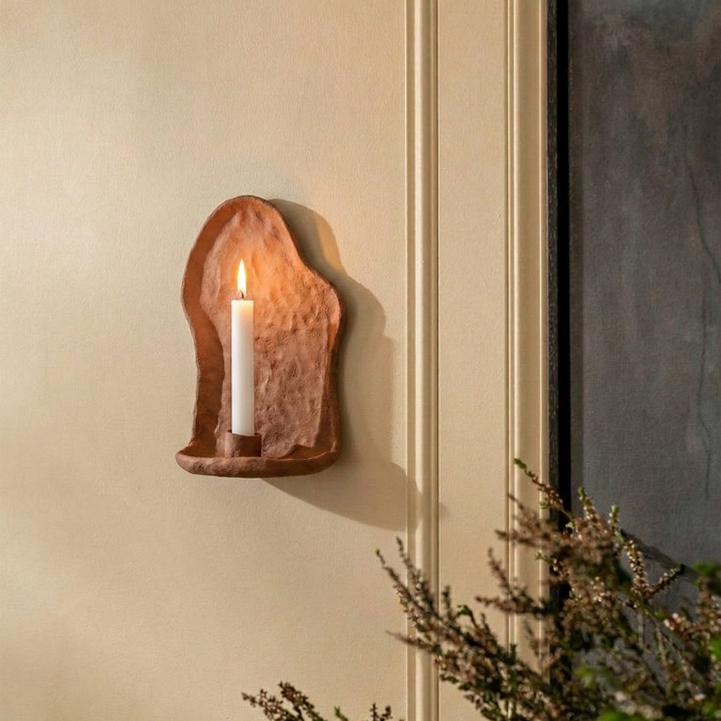 Wall-mounted candle holder with a candle on a beige wall.