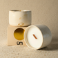 Two white ceramic candles on a beige surface with a cardboard box labeled 'um'.