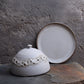 Ceramic dish with lace lid on a stone surface against a textured gray background