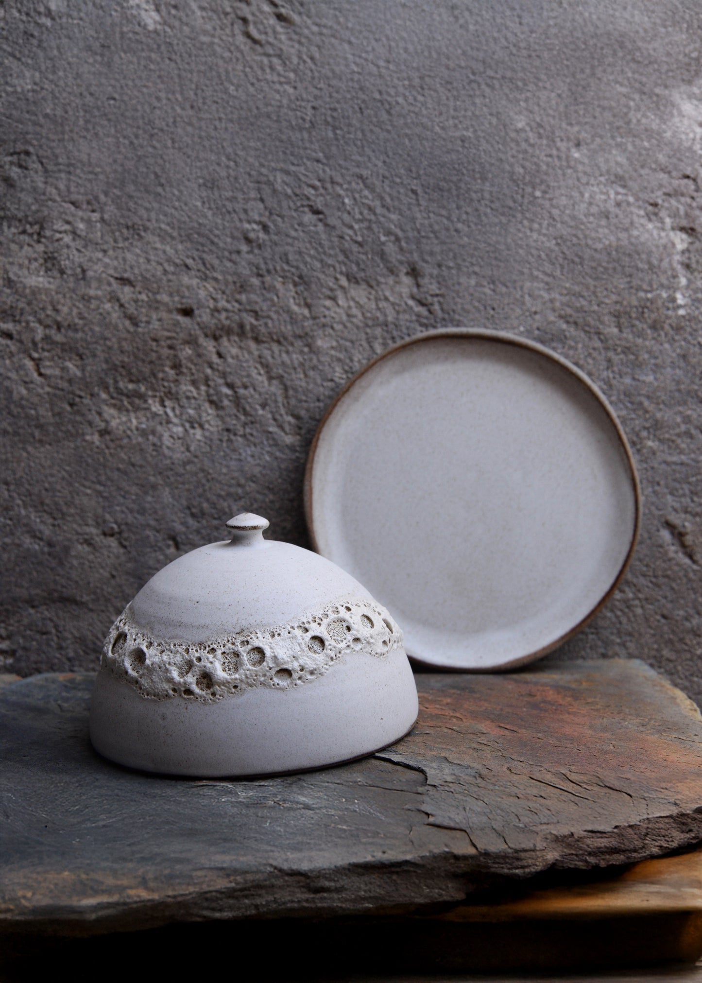 Ceramic dish with lace lid on a stone surface against a textured gray background