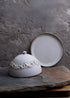 Ceramic dish with lace lid on a stone surface against a textured gray background