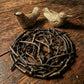 Two small bird figurines on a rustic wooden surface with a woven branch decoration.