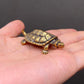The Enduring Wayfarer miniature brass turtle held in hand to show scale, with detailed shell pattern and warm aged patina, from the WILLAGE Tiny Objects collection
