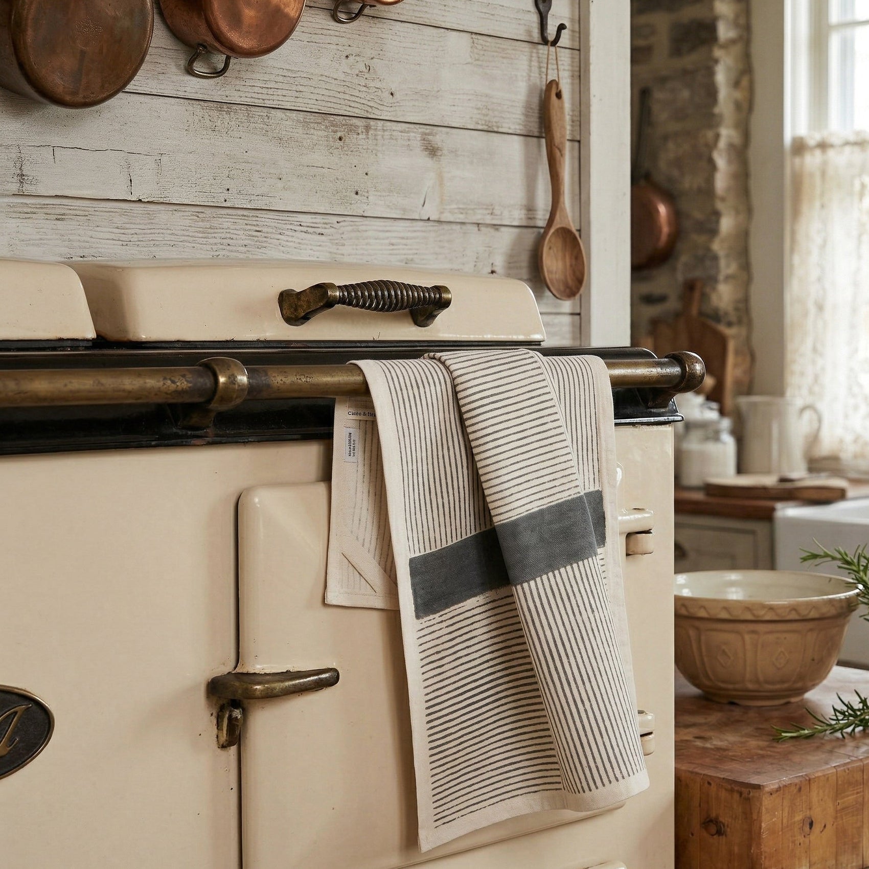 The Linear Slate kora cotton kitchen towel draped over a vintage oven handle in a rustic farmhouse kitchen, showing hand block printed linear design with slate-grey band on natural unbleached cotton