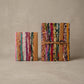 Two closed handmade journals with a multicolor cover woven from recycled sari cloth, tan leather strap with button, and a wrap tie ending in a heart-shaped charm