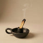 Black clay incense holder with a smoking incense stick on a beige background