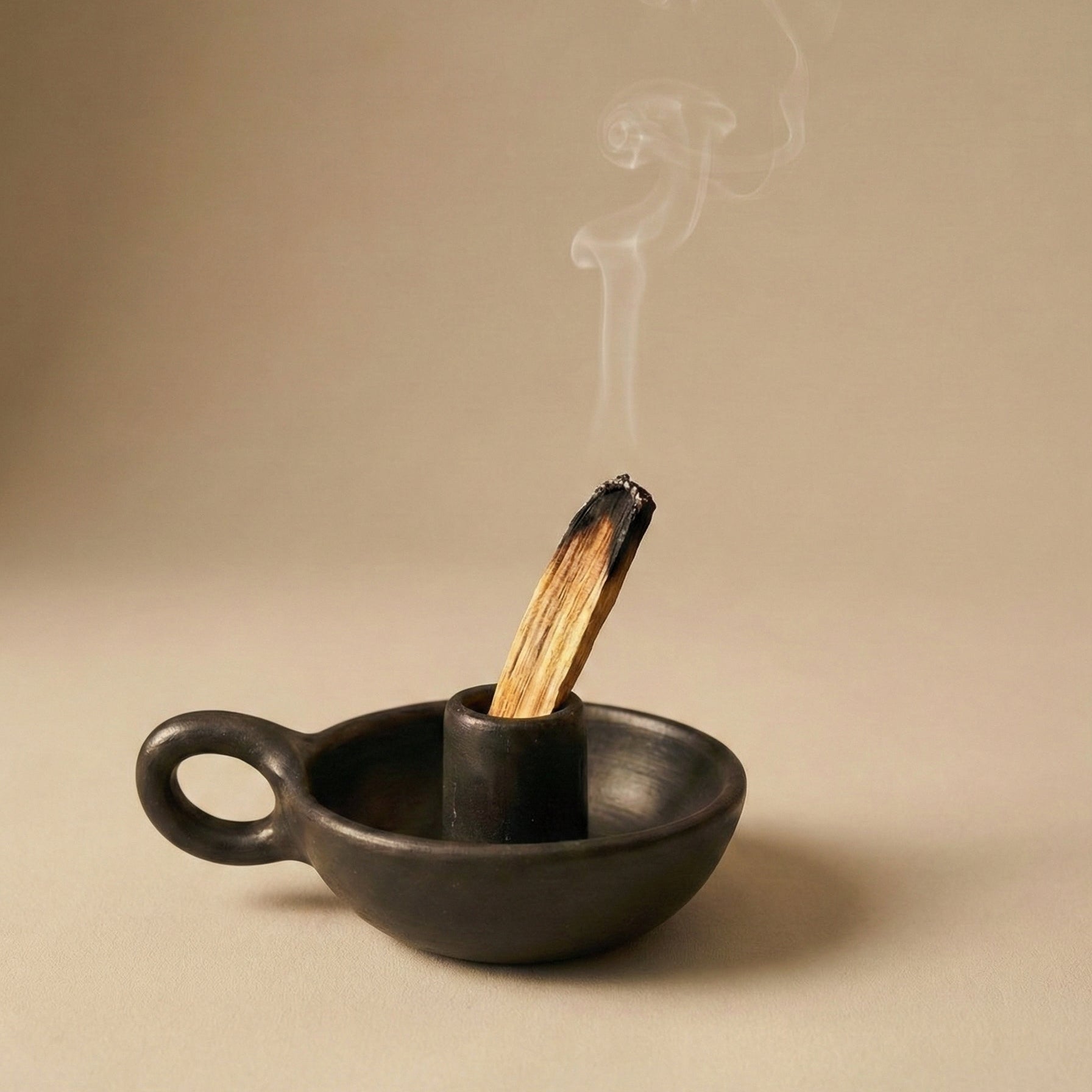 Black clay incense holder with a smoking incense stick on a beige background