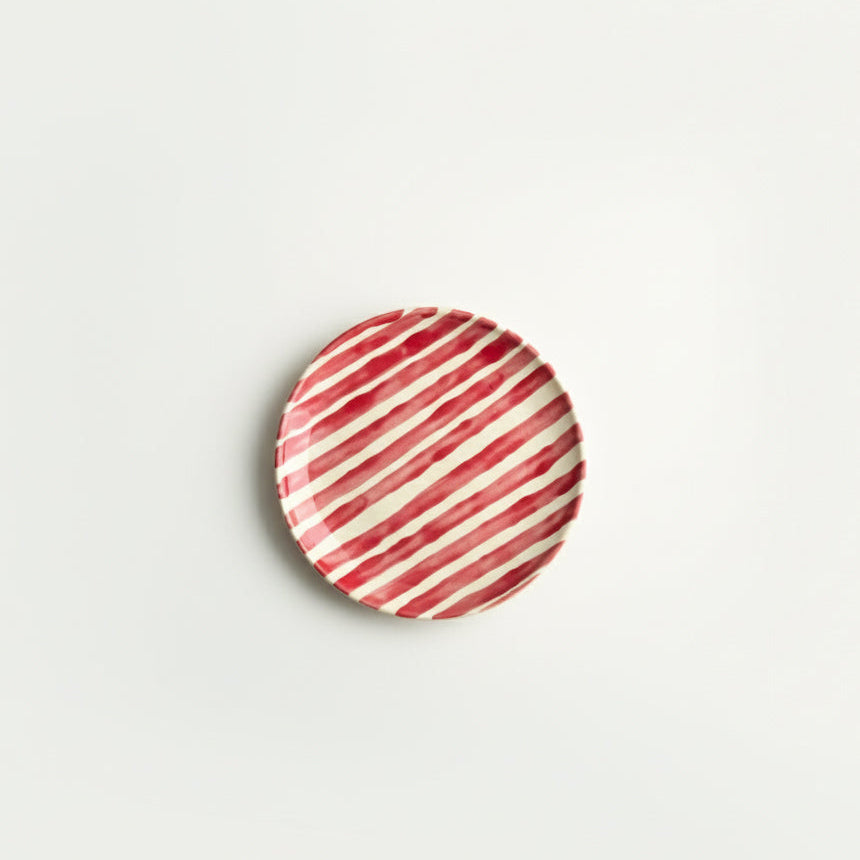 Round ceramic plate with red and white striped pattern on a light gray background