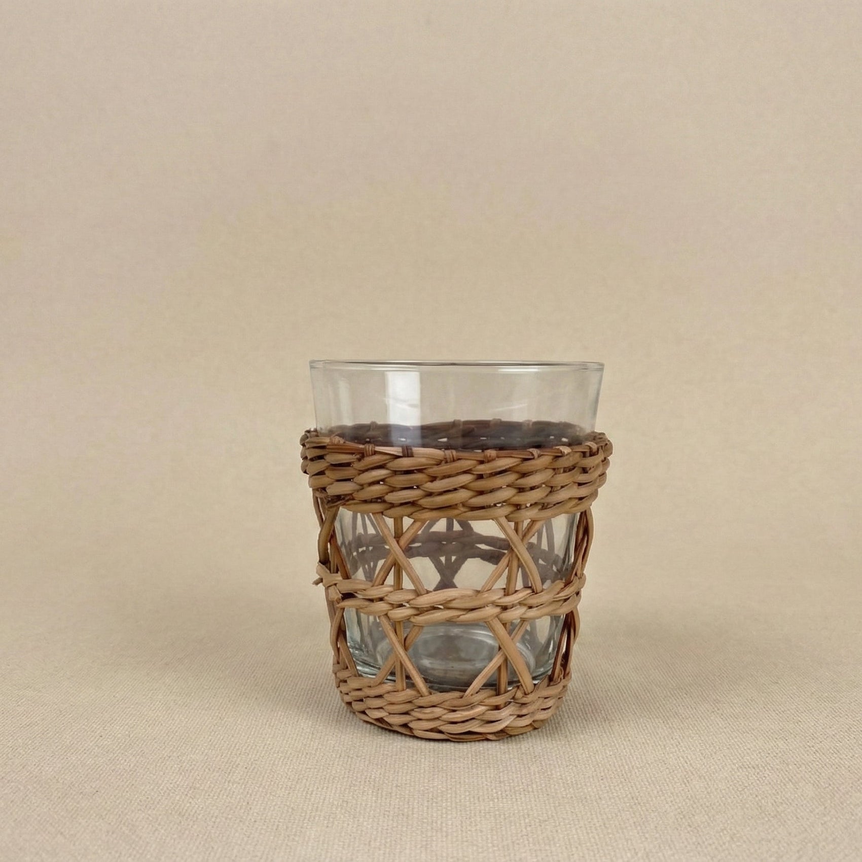 Clear glass with a wicker sleeve on a beige background