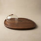 The Acacia Provision Board close-up showing acacia wood grain detail alongside the glass cloche dome and sculpted handle