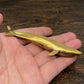 The Ancient Navigator miniature brass whale held in hand to show scale, with detailed flukes and textured patina, from the WILLAGE Tiny Objects collection.