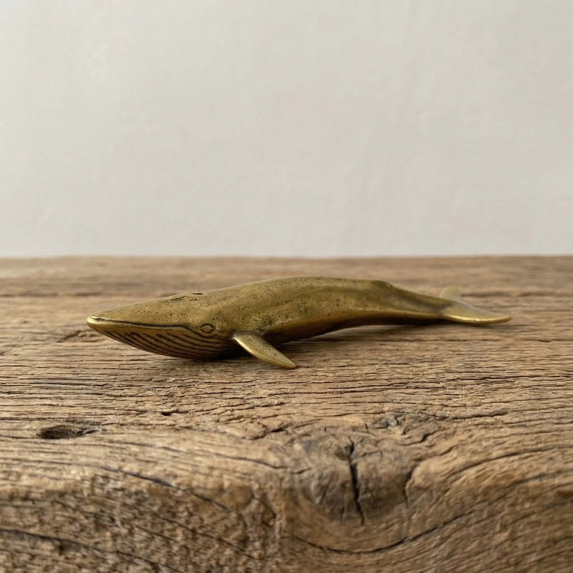 The Ancient Navigator miniature solid brass whale figurine with aged patina on natural stone surface
