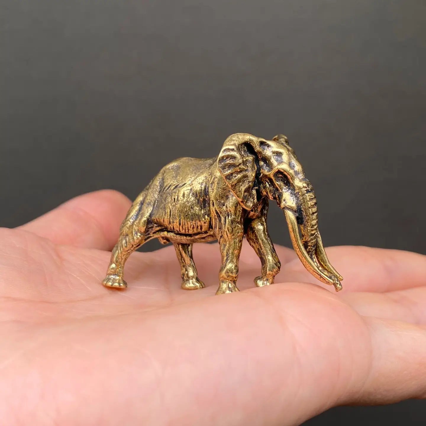 The Ancient Sage miniature brass mammoth held in hand to show scale, with detailed tusks and golden patina