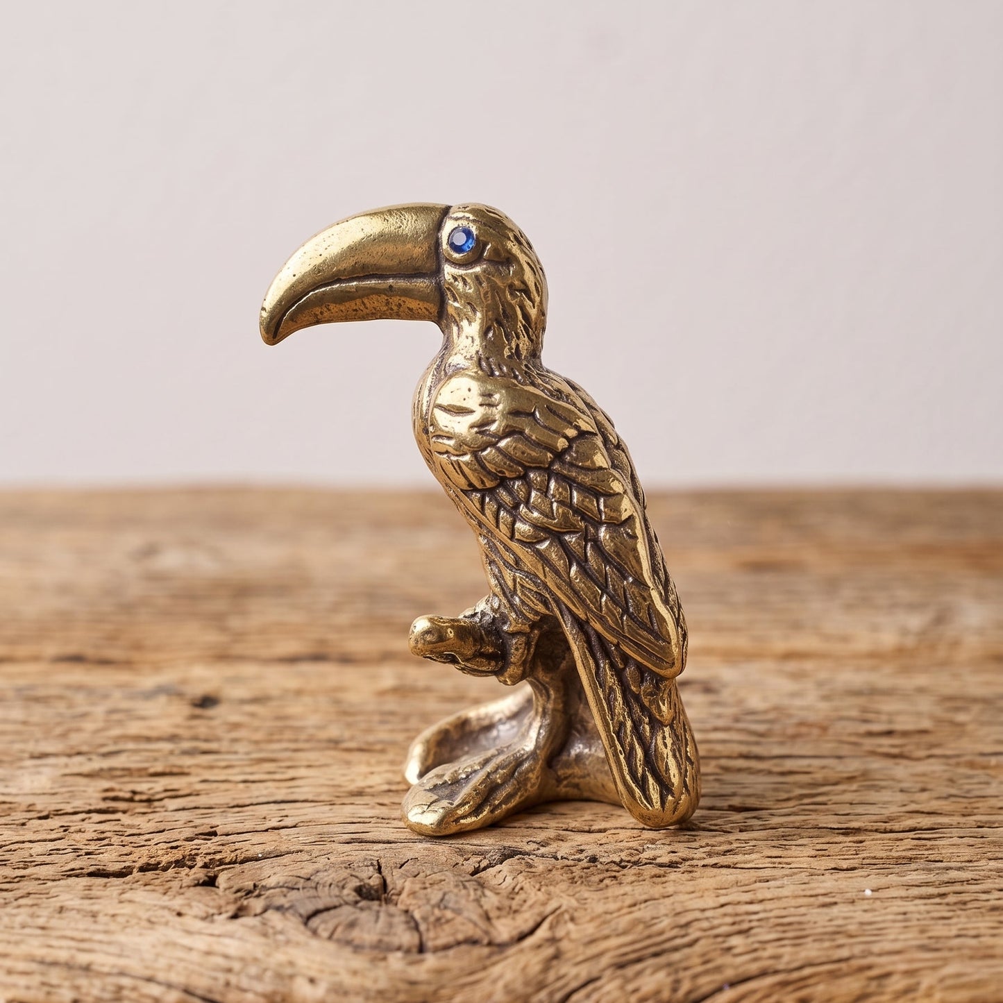 Brass toucan figurine standing on the corner of a rustic wooden table against a pale wall
