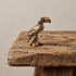 Small solid brass toucan figurine perched on a branch with a raised bill, fine feather detail and a blue stone eye, on weathered wood