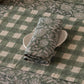 Block-printed linen napkin in Rio Green folded on a plate on a green gingham placemat, styled table setting with candlelight