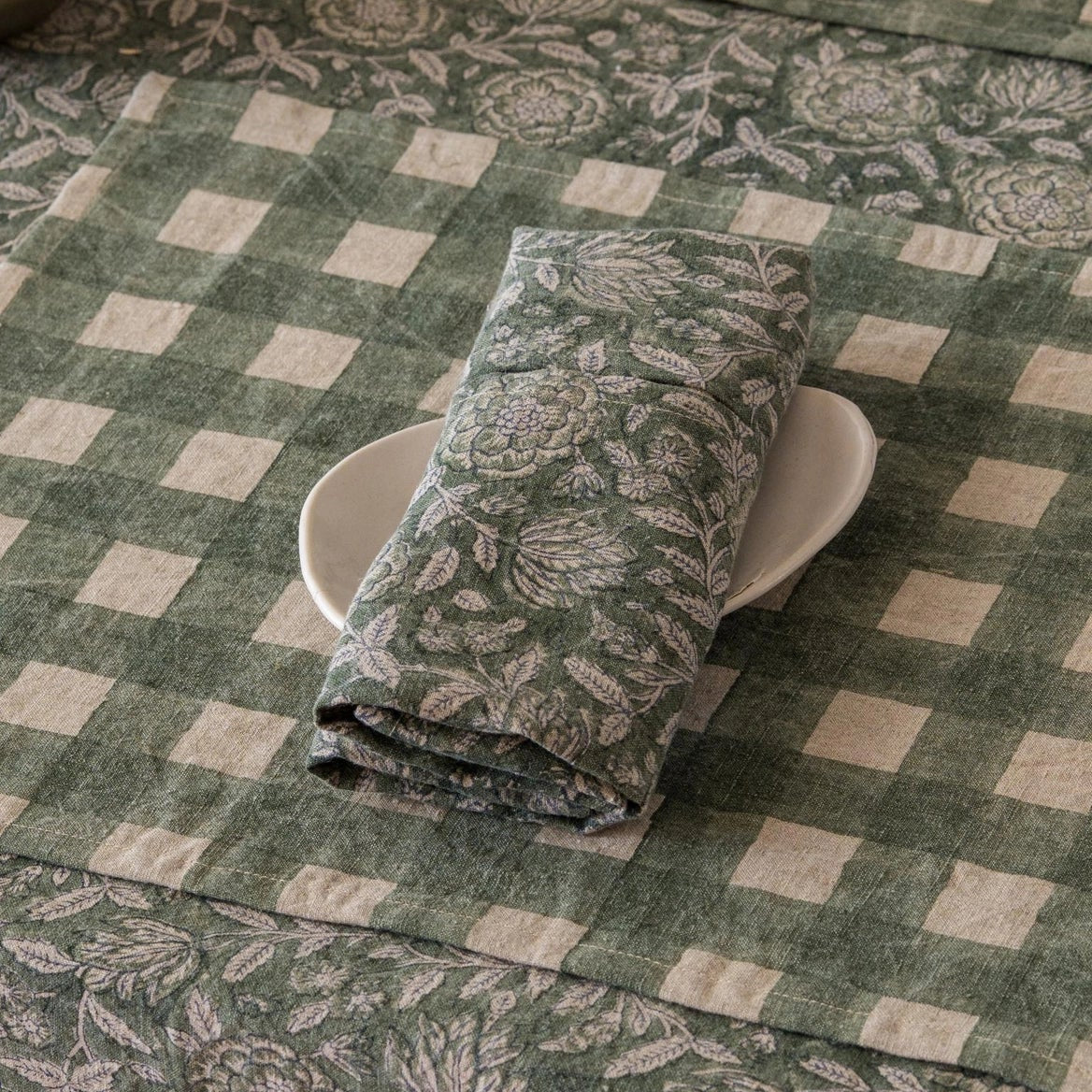 Block-printed linen napkin in Rio Green folded on a plate on a green gingham placemat, styled table setting with candlelight