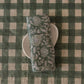 Block-printed European linen napkin in Rio Green botanical pattern folded on a white plate, showing peony and fern print detail, from WILLAGE