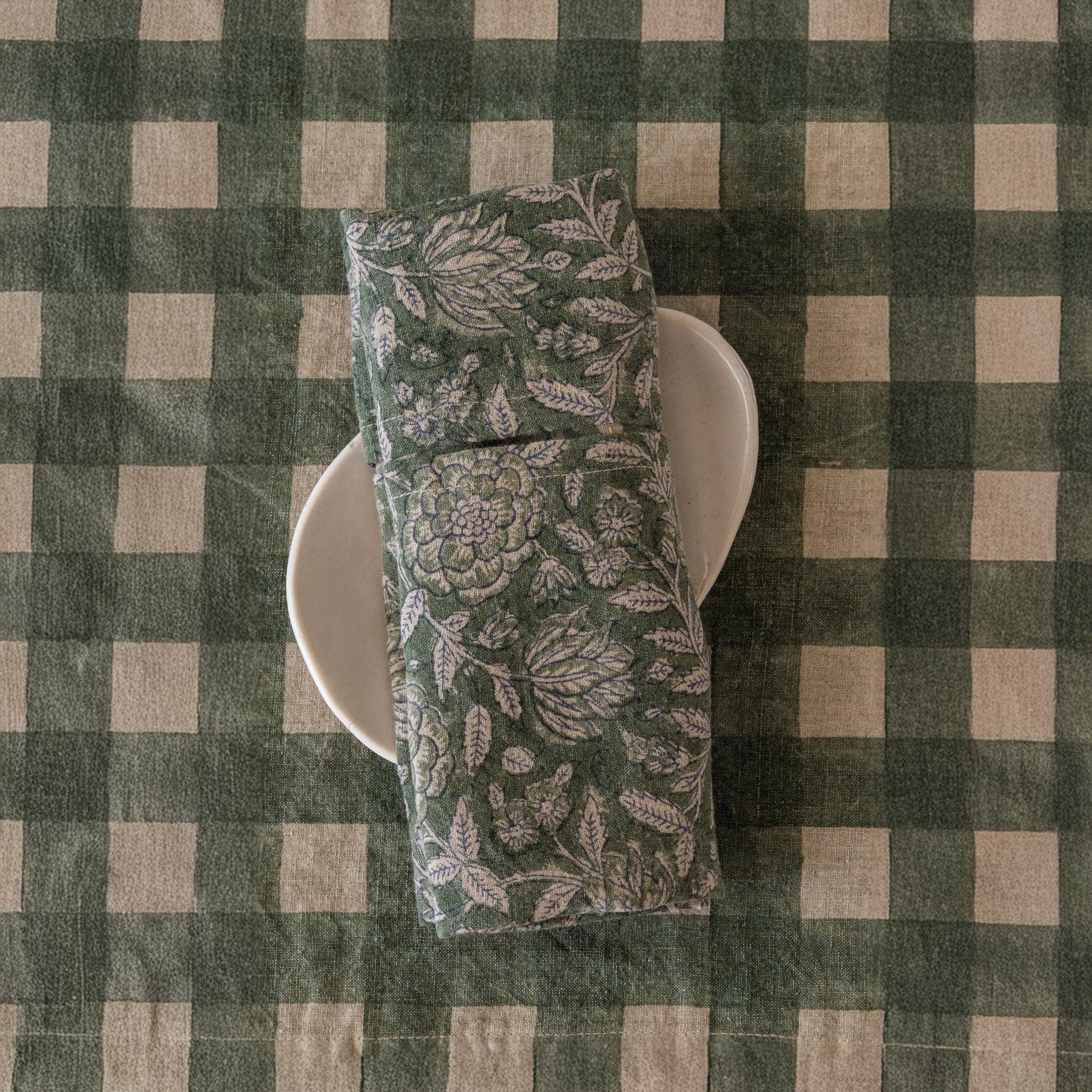 Block-printed European linen napkin in Rio Green botanical pattern folded on a white plate, showing peony and fern print detail, from WILLAGE