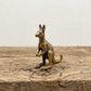 The Boundless Adventurer miniature brass kangaroo standing upright on a wooden surface, with warm aged patina, from the WILLAGE Tiny Objects collection