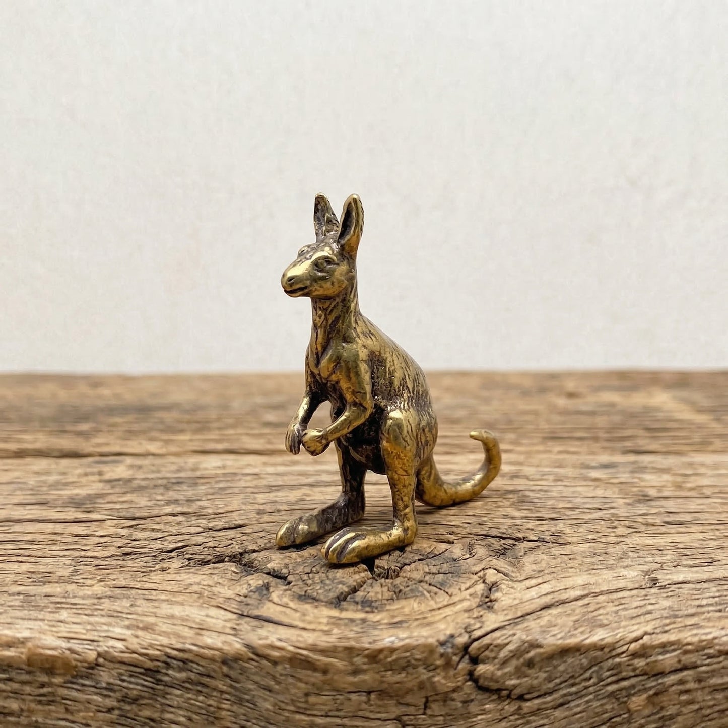 The Boundless Adventurer miniature brass kangaroo standing upright on a wooden surface, with warm aged patina, from the WILLAGE Tiny Objects collection