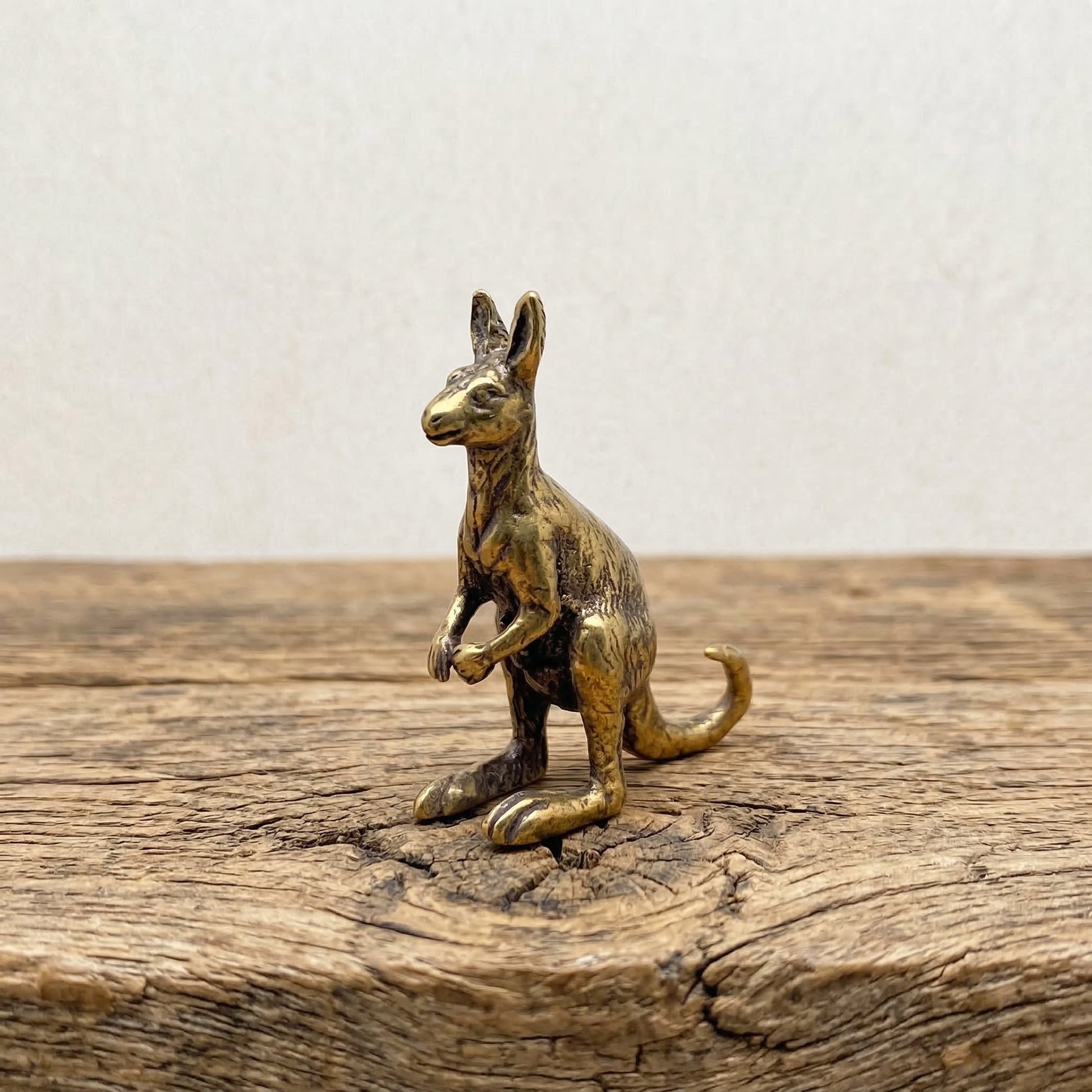 The Boundless Adventurer miniature brass kangaroo standing upright on a wooden surface, with warm aged patina, from the WILLAGE Tiny Objects collection
