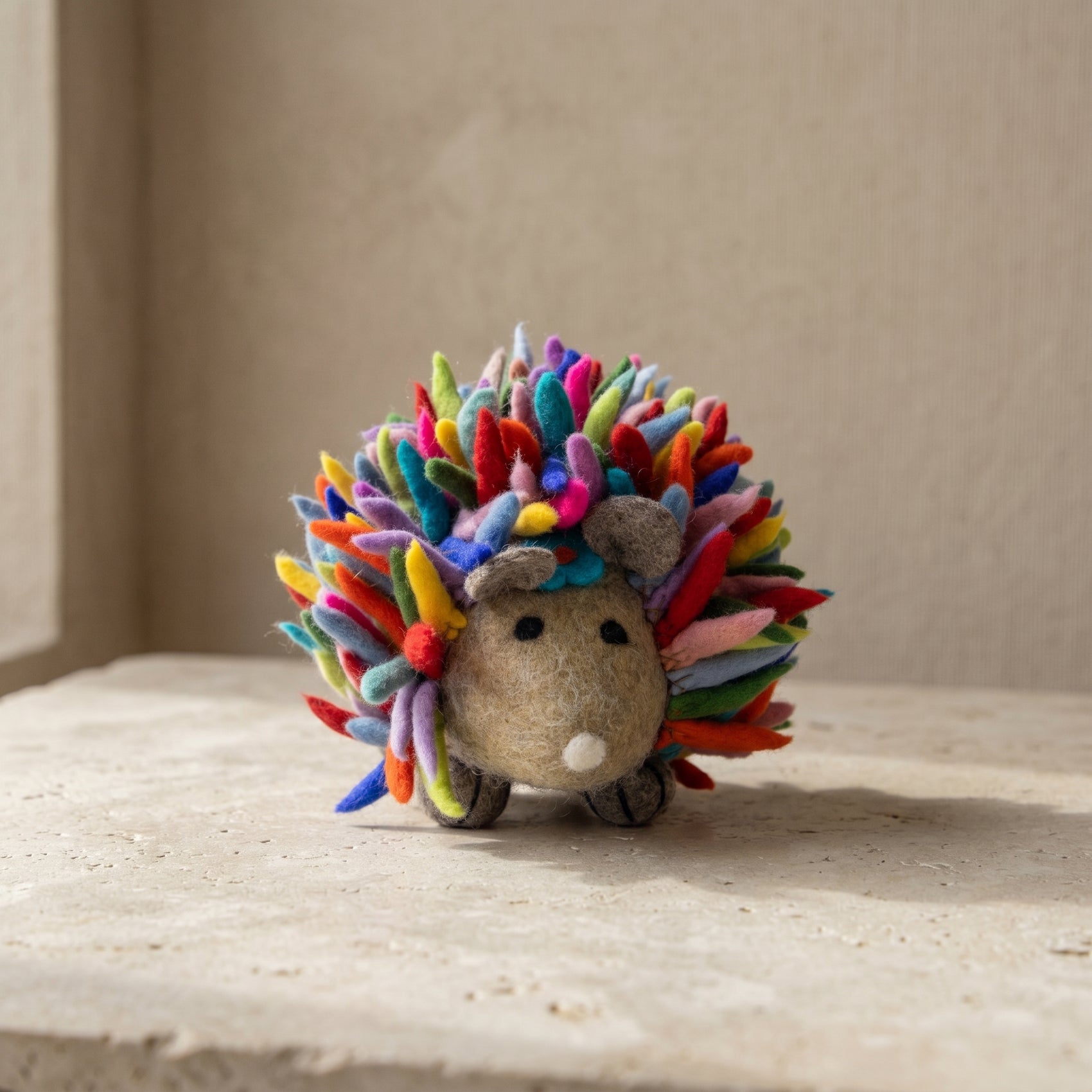 Hand-felted rainbow hedgehog soft toy with multicolored wool spines and a grey felt face, made in Nepal
