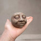  Concrete head sculpture resting in an open palm to show its size, with the word Sing pressed into the back Glow_ Stone 